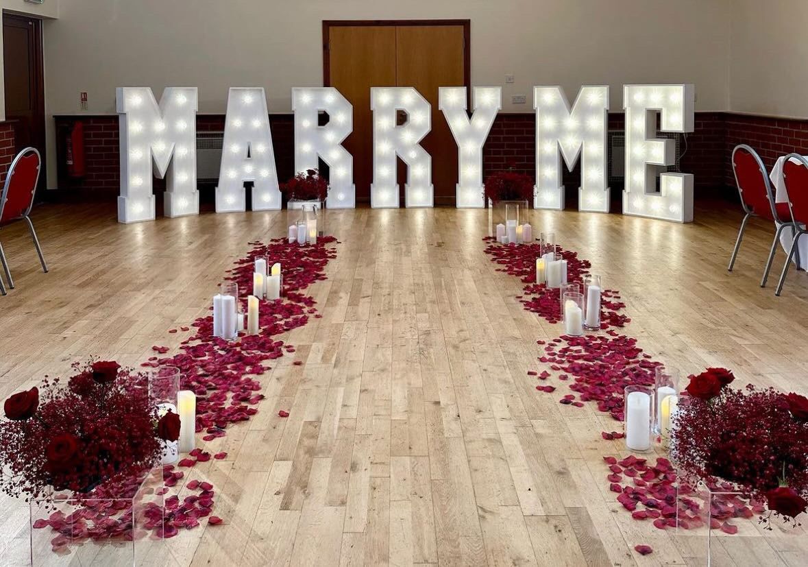 Marquee letters spelling MARRY ME with rose petal aisle